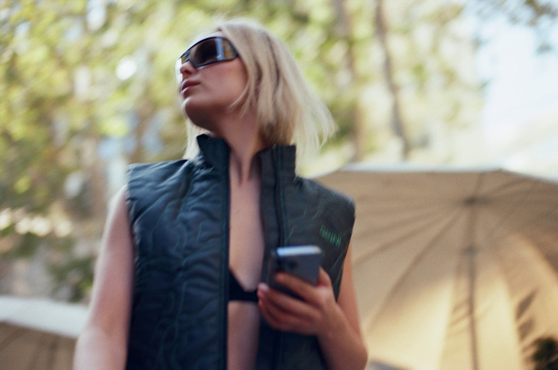 a woman in a black dress and sunglasses looking up at an umbrella